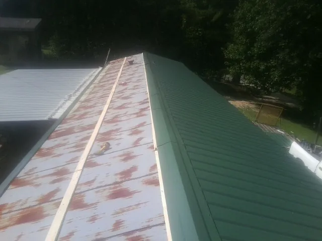Old rusted panels beside newly installed green metal roofing — Wind Damage Roof Repair by Roofing Brothers in Wells