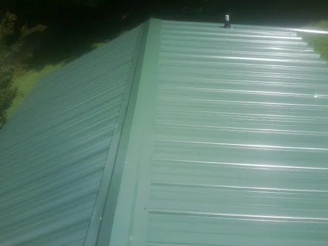 New green metal panels meeting at the ridge of a roof — Flat Roof Repair work by our crew in Wells