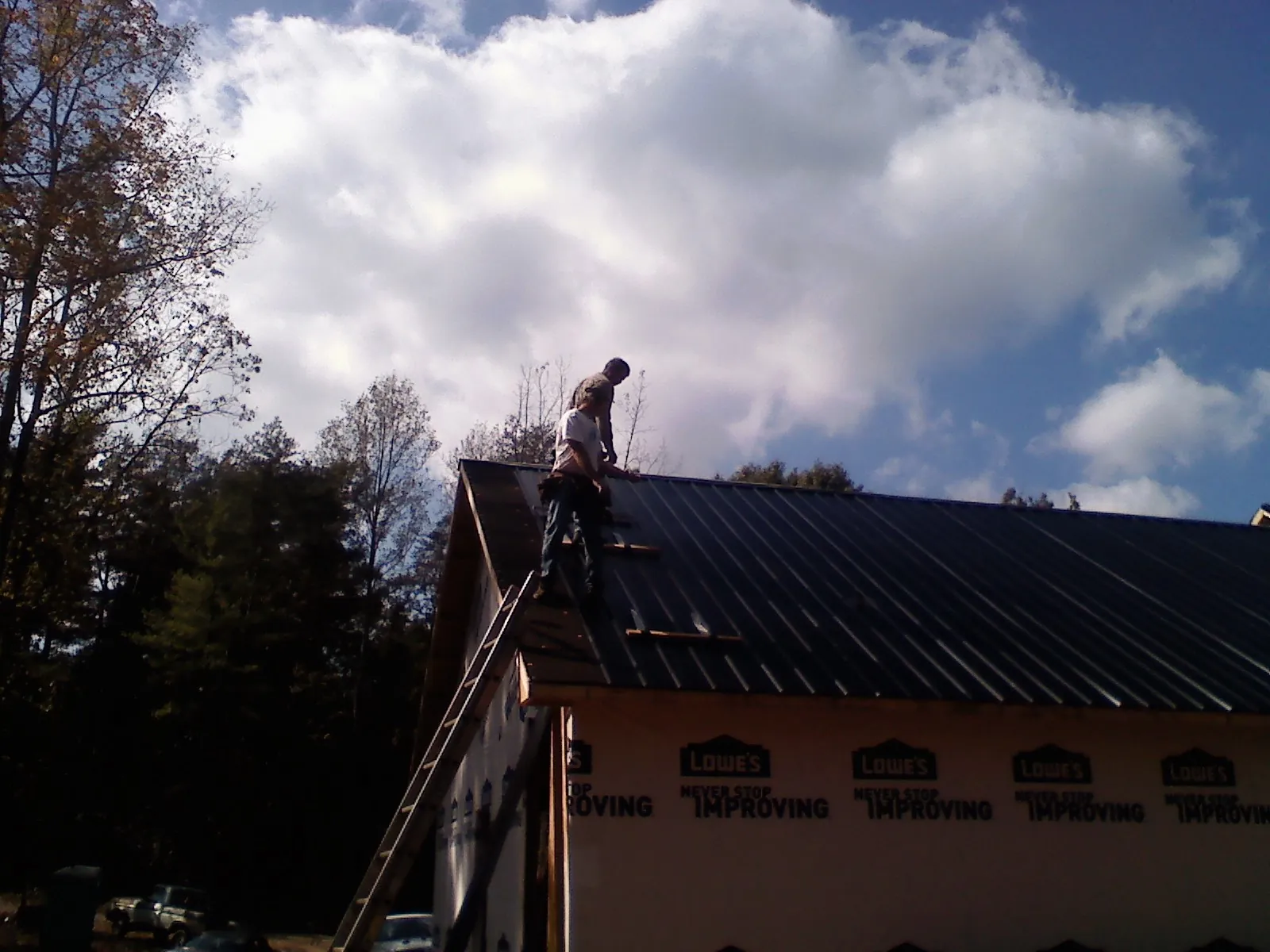 Roofer fastening dark metal panels high against a cloudy sky, from a Roof Inspection job in Wells